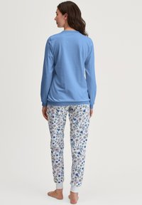 Blauwe lange mouwen top met ronde hals, gecombineerd met witte pyjamabroek met een meerkleurig bloemenpatroon en geribde boorden bij de enkels.