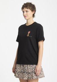 Camiseta de algodón negra de manga corta, con un gráfico colorido de una piña y el texto "volcom". Combinada con una falda de leopardo con pliegues.