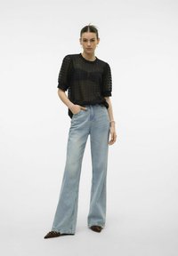 Top negro de punto abierto con mangas cortas, combinado con vaqueros rectos de color azul claro. Los accesorios notables incluyen una pulsera y zapatos marrones de punta.