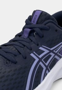 Marineblå løpesko laget av pustende mesh, med hvit mellomsåle, lilla aksenter og teksturerte lisser med en logo på tungen.