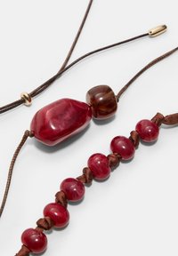 Czerwony naszyjnik z koralików z gładkimi, błyszczącymi kamieniami w różnych kształtach, nawleczony na brązowy sznurek, z złotym akcentem.
