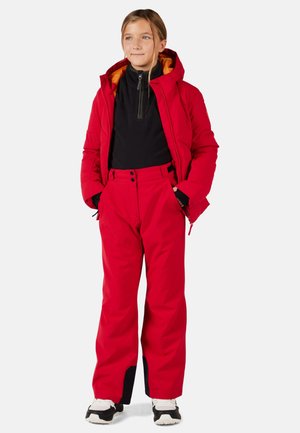 Giacca isolante rossa con cappuccio, abbinata a pantaloni da sci rossi e una maglietta nera. Caratterizzata da cerniere, tasche e accenti a contrasto.