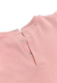 Prenda rosa de manga corta con escote redondeado, que cuenta con botones a presión plateados a lo largo de la tapeta y una tela suave y texturizada.