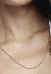 Collana delicata in oro posata su pelle nuda, con un design sottile e semplice e una texture liscia, che mette in risalto una lucentezza sottile.