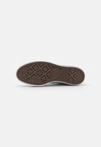 Sole od námořnicky modrého tenisu Converse s hnědou texturovanou gumovou podrážkou a bílou mezipodrážkou na čistém bílém pozadí.