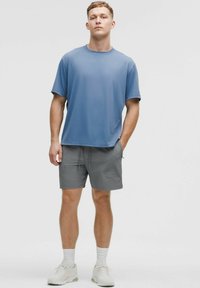 Kortærmet blå T-shirt lavet af blødt stof, parret med lys grå shorts med elastisk liv og sidelommer. Sneakers fuldender looket.