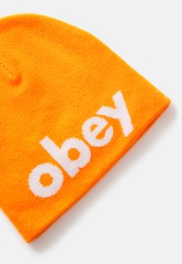 Orange knit beanie featuring a white embroidered text "obey." The material is soft with a smooth texture, and the design is simple and versatile.