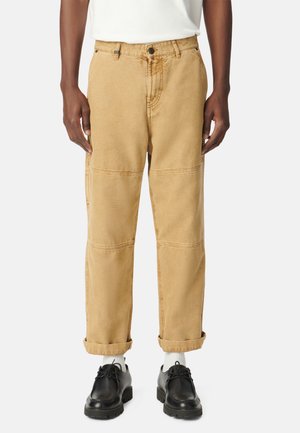 Pantaloni cargo khaki con vestibilità dritta, dettagli cuciti e orli arrotolati. Abbinati a scarpe nere e calze bianche, su uno sfondo neutro.