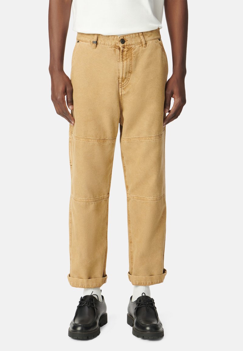 Pantalones cargo color caqui con un corte recto, detalles de costura y puños enrollados. Combinados con zapatos negros y calcetines blancos, sobre un fondo neutral.