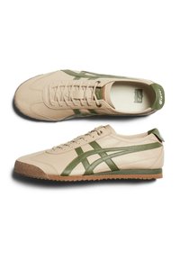 Beige leather sneakers with green accents and striped design. Features textured rubber sole and lace closure. Classic athletic style.