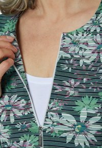 Blumige Zip-Up-Bluse mit navy gestreiftem Grund, die weiße und lila Blumen zeigt. Sichtbarer Reißverschluss und weiße innere Schicht sind sichtbar.