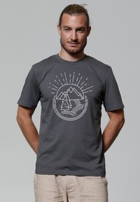 Grijze katoen t-shirt met een witte grafische print van bergen, een boom en zonnestralen in een cirkelontwerp aan de voorkant.
