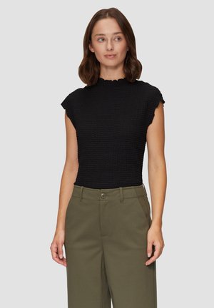 Haut noir à manches courtes avec un tissu texturé et froncé, doté d'un col montant et de bords festonnés, associé à un pantalon vert olive.