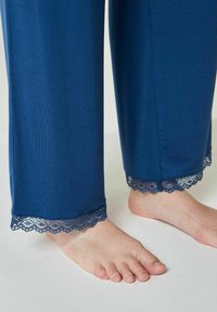 Navyblauwe broek met een zachte textuur, voorzien van een delicate kantafwerking aan de zoom. Geëtaleerd met blote voeten voor context.