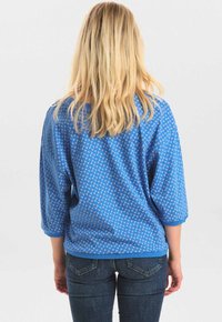 Blå mönstrad skjorta med lös passform, 3/4-långa ärmar och rund halsringning, tillverkad av mjukt tyg med en strukturerad yta.