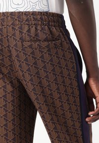 Bruna mönstrade joggers har en geometrisk design, elastisk midja, sidostrips och en liten ficka bak. Texturerat tyg.