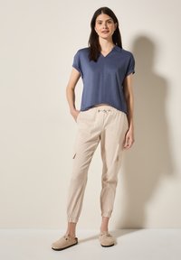 Haut bleu marine à manches courtes avec col, associé à un pantalon cargo beige fuselé avec des poignets élastiques et des poches, porté avec des sabots beiges.