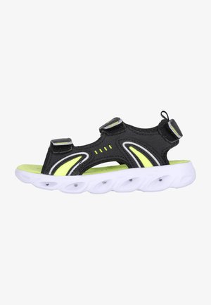 Schwarze Sandale mit einem Obermaterial aus Mesh, neon-gelben Akzenten, zwei Velcro-Riemen und einer weißen, strukturierten Sohle mit Luftpolstern für Dämpfung.