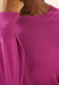 Pull en tricot fuchsia avec col rond, poignets côtelés, et une texture douce, avec une silhouette ajustée et une finition lisse.