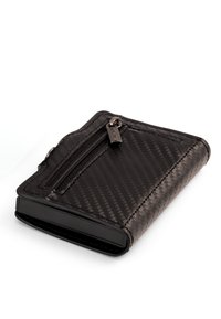 Mustassa tekstuurilla varustettu lompakko, jossa on vetoketjullinen tasku edessä, suljettuna ja lepäämässä valkoisella pinnalla.