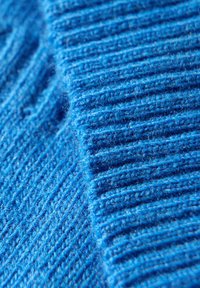 Blauer Strickstoff mit feiner gerippter Textur und sichtbaren Fasern, der eine lebendige, gleichmäßige Farbe und ein durchgängiges Muster auf der Oberfläche zeigt.