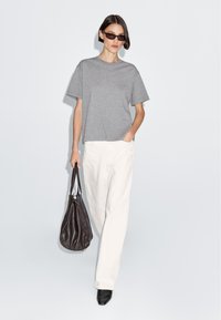 Grå oversized t-shirt, hvide brede bukser, sorte spidse sko og en mørkebrun slouchy håndtaske, med mørke solbriller.