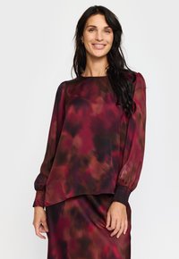 Rød og brun bluse med abstrakt mønster, lange ermer, elastiske mansjetter og løs passform. Glatt, lett stoff; rund hals.