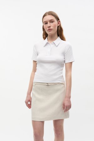 White short-sleeve polo shirt with a collar and three buttons, paired with a light beige mini skirt featuring a subtle texture and belt detail.