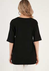 Black ribbed tunic shirt with a loose fit, short sleeves, wide neckline, and a straight hem, designed for comfort and ease of movement.