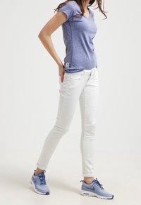 Camiseta morada jaspeada con escote en V y mangas cortas, combinada con jeans ajustados blancos y zapatillas deportivas de color azul claro, con detalles de cordones.