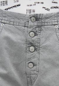 Γκρι σορτς από ύφασμα με ψηλή μέση, κούμπωμα με πέντε κουμπιά και μεταλλικά διακοσμητικά. Η υφή φαίνεται μαλακή με ελαφρώς τσαλακωμένο φινίρισμα.