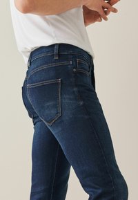 Blauwe denim jeans met een slim fit, met oranje stiksels, twee achterzakken en een vervaagde textuur. Draag ze met een plain wit shirt.