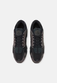 Svart och mörkgröna sneakers med mesh- och mockamaterial, snörningsdesign, perforerade sektioner och en cirkulär logotyp på tungan.