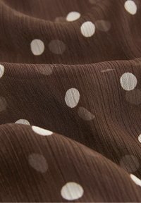 Tissu marron à la texture douce, orné de grands pois blancs et de légères rayures verticales, créant une apparence à la fois superposée et fluide.