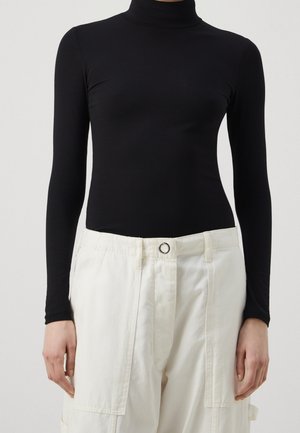 Haut noir à col roulé ajusté avec manches longues, associé à un pantalon cargo blanc. Le haut est en tissu lisse, le pantalon a une coupe décontractée avec des poches.