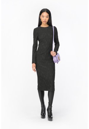 Robe noire à manches longues côtelées avec des rayures verticales, associée à un sac bandoulière lavande. Le mannequin porte des bottines à plateforme noires brillantes.