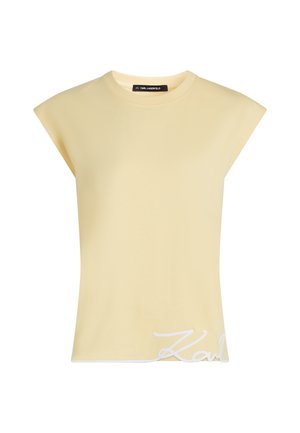 Αμάνικη ανοιχτοκίτρινη μπλούζα με ενισχυμένους ώμους και λευκό κείμενο με γραφή σε στυλ καλλιγραφίας κοντά στο δεξί κάτω τελείωμα.