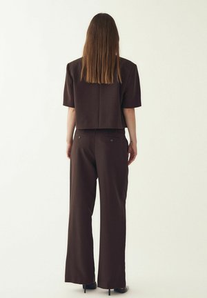 Pruun lühike t-särk lühikeste varrukatega, mis on kombineeritud pruunide laiade pükstega, millel on peen tekstuur ja tagatasku detailid.