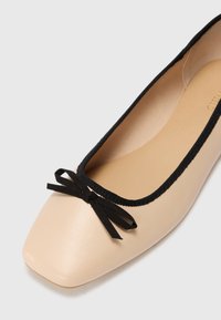 Ballet flats in a nude shade with a square toe, black ribbon trim, and a bow detail at the front. Smooth leather material.