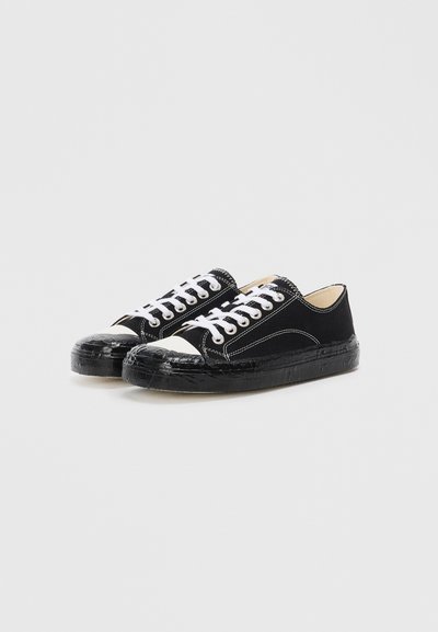 Black canvas sneakers with white laces and stitching, featuring a rounded white rubber toe cap and a textured black rubber sole.