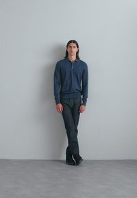 Mörkblå långärmad pikétröja ihop med grå jeans och svarta skor. Tätt sittande design med ribbade muddar och klassisk krage.