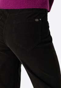 Black corduroy trousers with a straight cut, featuring a diamond-shaped rear pocket and a small metallic brand tag on the waistband.
