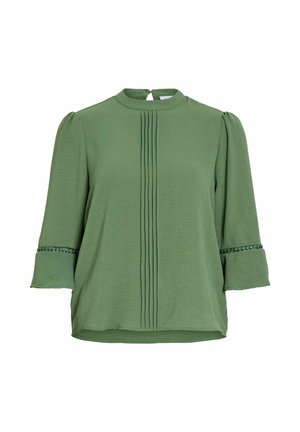 Blouse verte avec des plis verticaux sur le devant, manches 3/4 avec bordure en dentelle au-dessus des poignets évasés, et petite fermeture par bouton au dos.