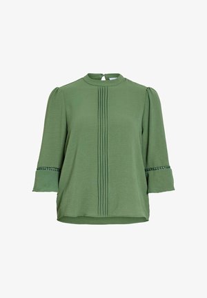 Blouse verte avec des plis verticaux sur le devant, manches 3/4 avec bordure en dentelle au-dessus des poignets évasés, et petite fermeture par bouton au dos.