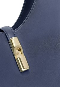 Borsa in pelle blu navy con una texture liscia, caratterizzata da una chiusura in metallo dorato. La cucitura è ordinata e il design è minimalista.