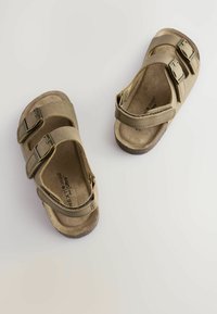 Brune og beige sandaler med to justerbare remme og metalliske spænder, der har en blød, tekstureret sål og en let fodsål.