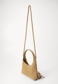 Sac à main en suède beige avec une anse tressée, une poignée circulaire et des franges latérales. Il présente un design minimaliste et une texture lisse.