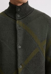 Dark green knitted cardigan with a high collar, featuring textured panels and diagonal yellow stripes, buttoned with matching gray buttons.