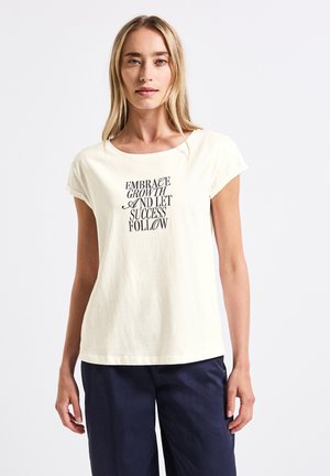T-shirt crème à manches courtes en coton avec un col rond ; présente un design de texte noir : "Acceptez la croissance et laissez le succès vous suivre."