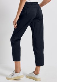 Pantalones cortos de color azul marino con una cintura elástica, dos bolsillos traseros y una textura suave. Combinados con zapatillas blancas.